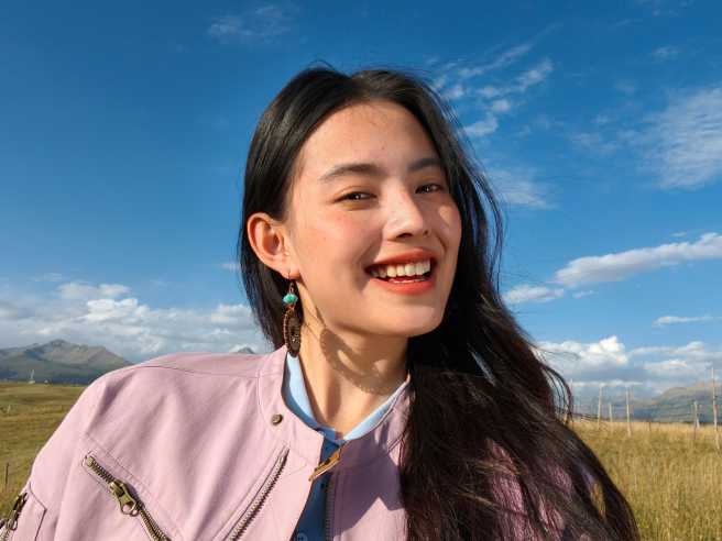 Radiant outdoor selfie of a smiling woman, captured by 50MP Luminous Selfie Camera