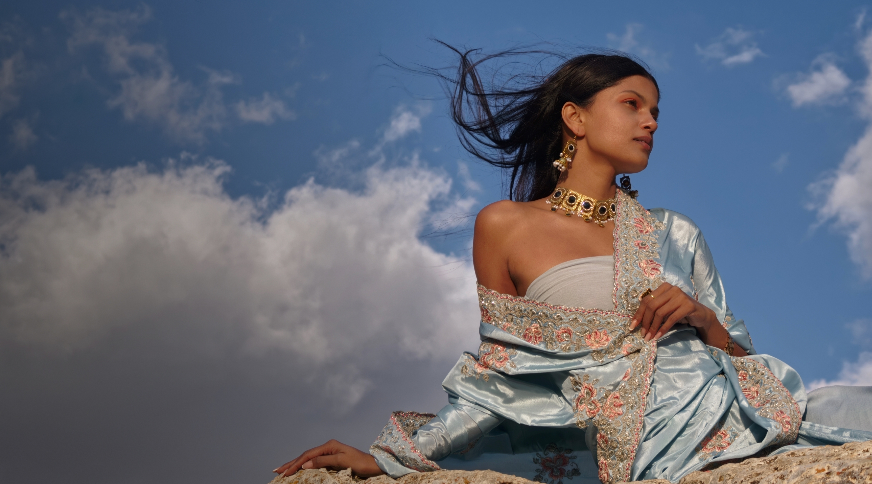 Woman in a blue embroidered dress against a bright sky, showing natural color from LUMO True Color Engine