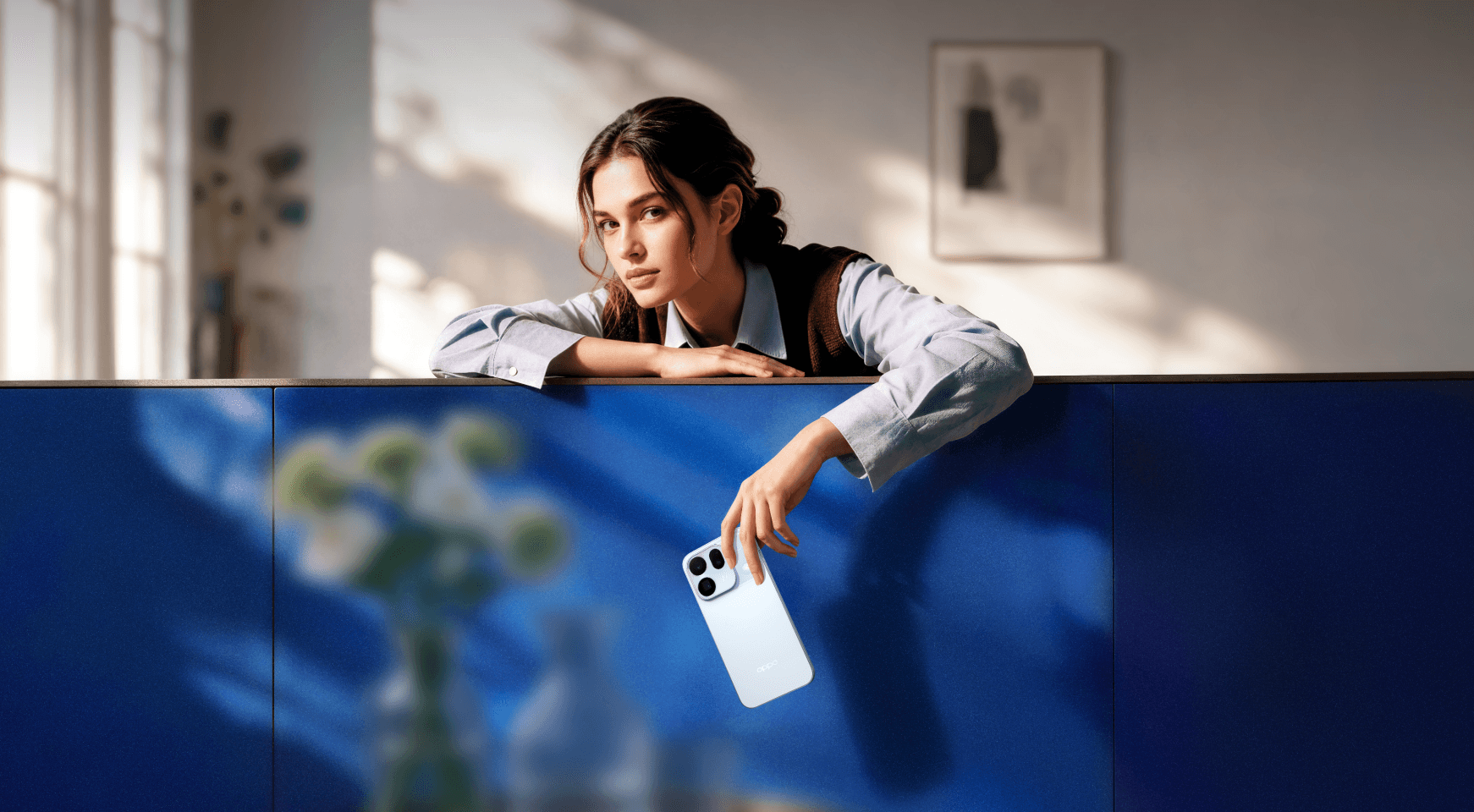 امرأة تحمل هاتف OPPO Find X10 بلون Glacier Blue في غرفة تغمرها أشعة الشمس