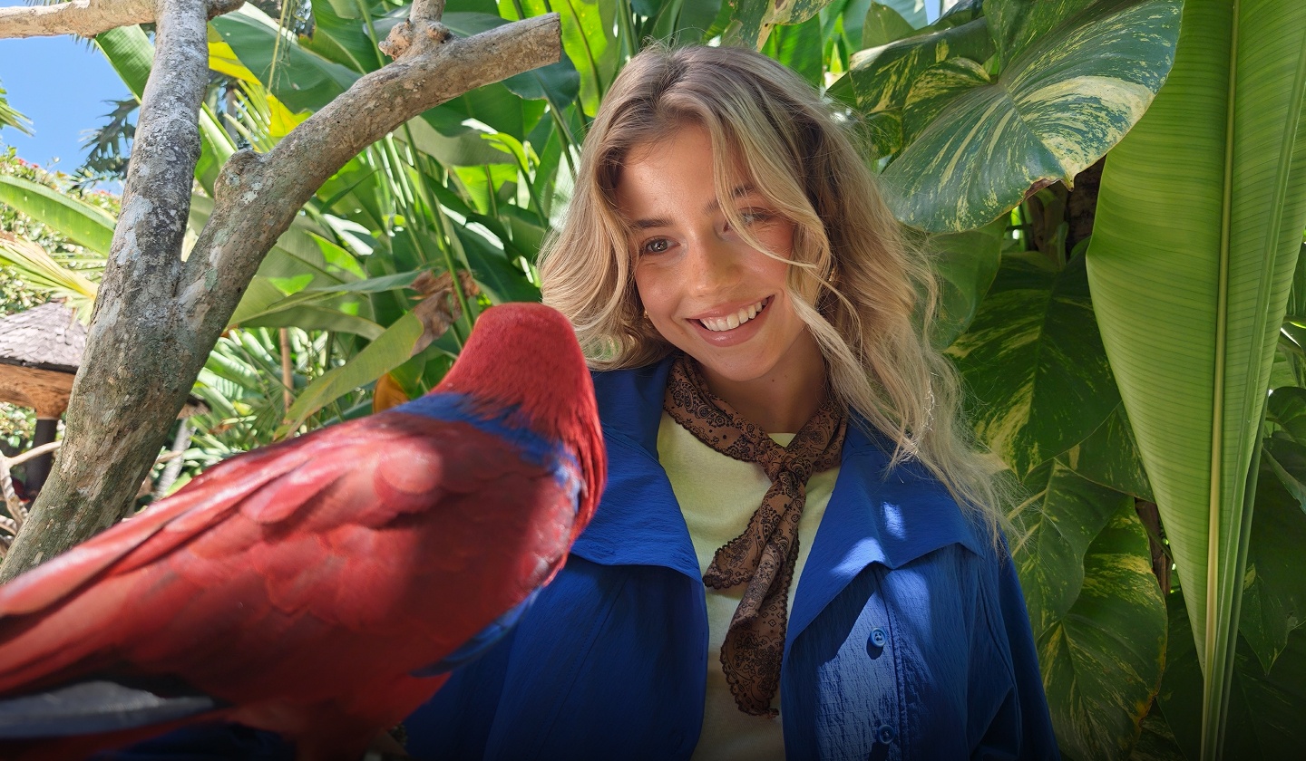 Detailed smartphone shot of a vibrant red parrot and a smiling woman, showcasing motion photography of OPPO Find X10