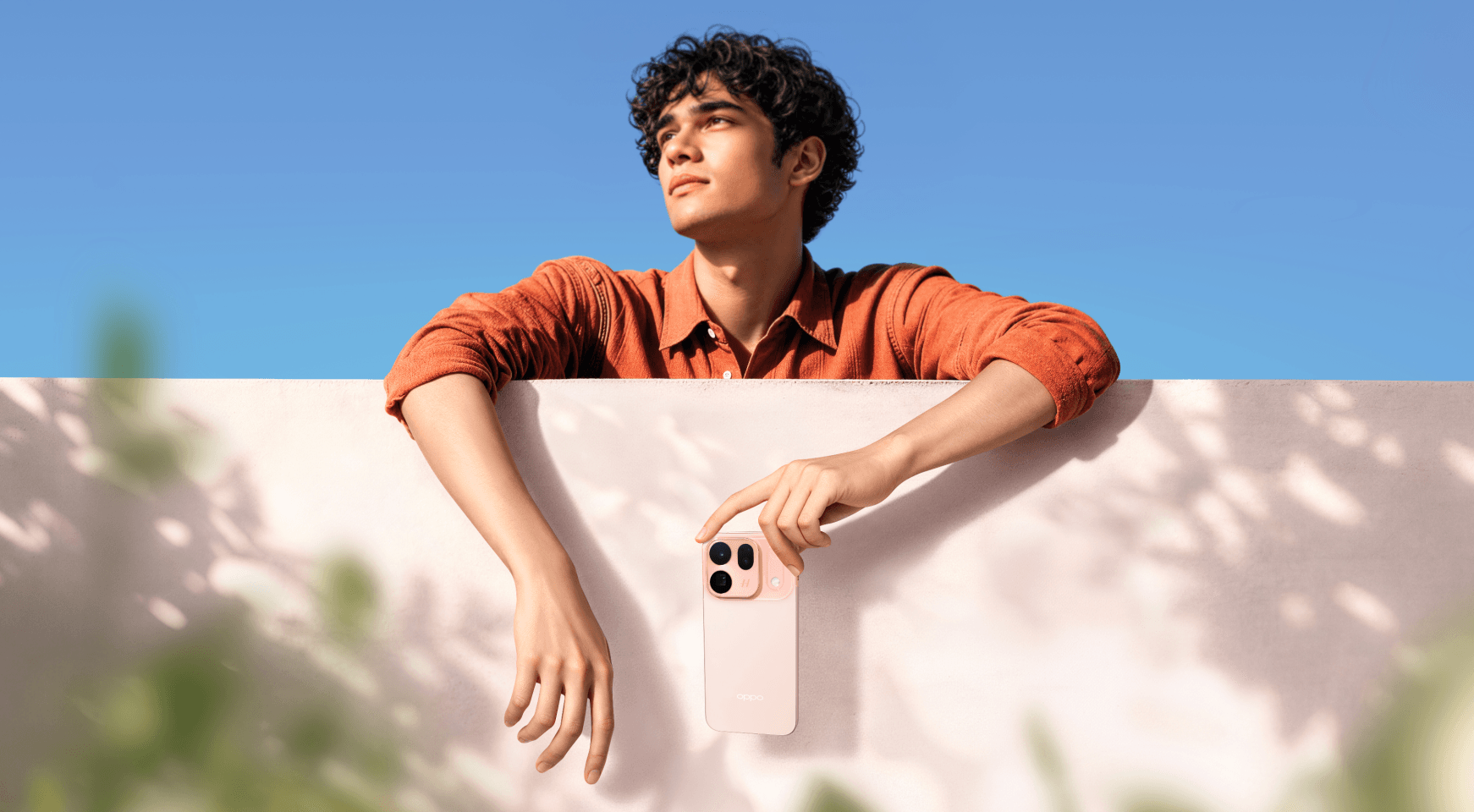Young man holding the OPPO Find X10 in Glow Coral against a sunlit wall