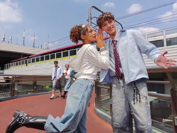 A playful photo of a woman whispering to a man on a bridge, with a train and pedestrians in the background