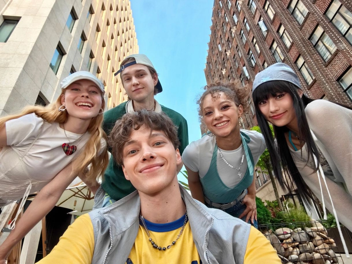 Five friends smiling against a city backdrop in a 0.6x ultra-wide selfie