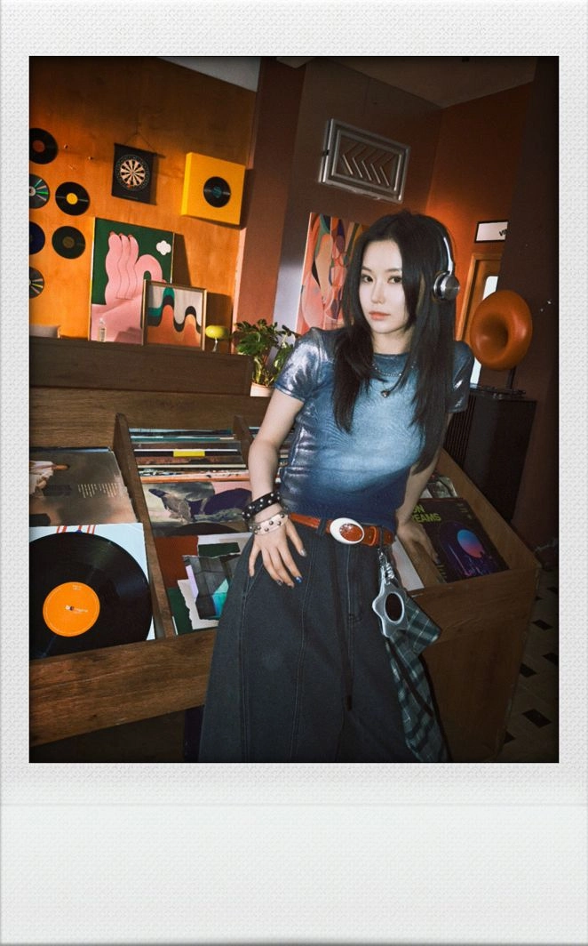 A retro Polaroid-style portrait of a girl in a record store, framed with a white instant film border